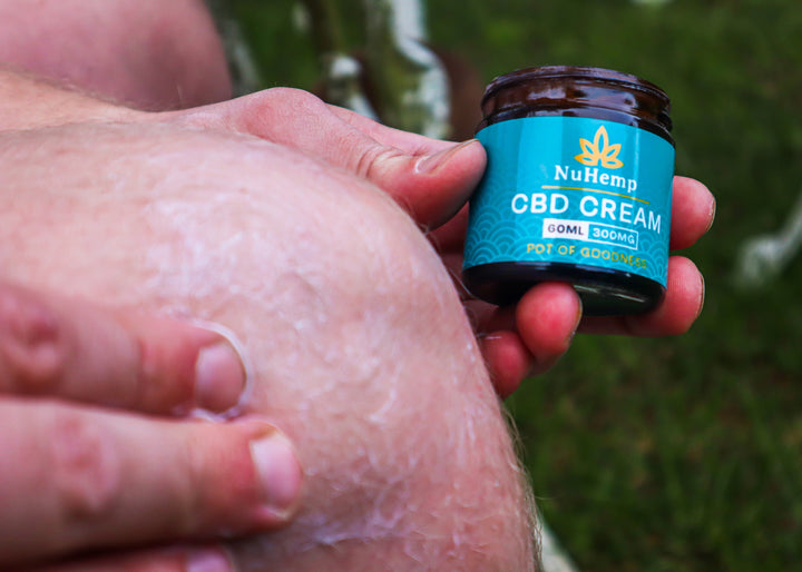 man in field holding up a cbd cream tub to the camera